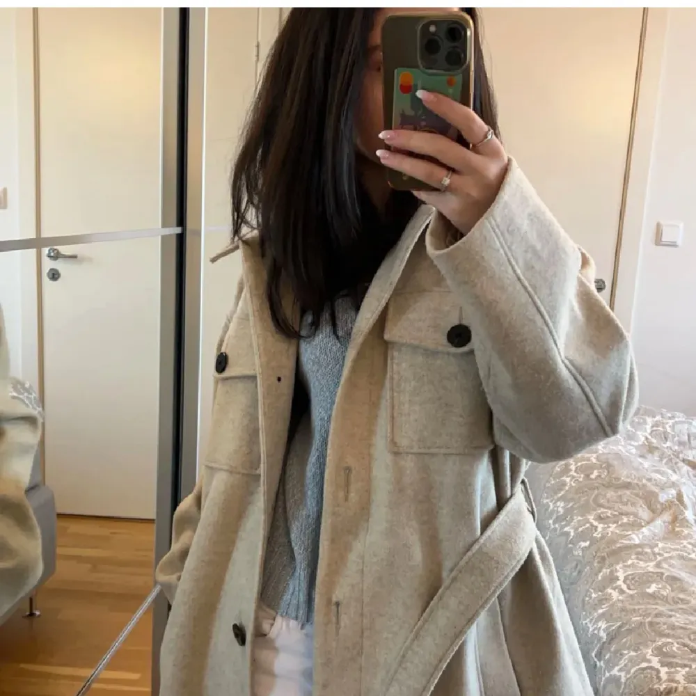 Säljer en superfin beige kappa med bälte i midjan. Den har stora knappar och två bröstfickor som ger en snygg look. Perfekt för höst och vår när det är lite kyligt ute. Kappan är långärmad och har en klassisk krage.. Jackor.