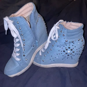 Blå sneakers med kilklack och nitar - Säljer ett par coola blå sneakers med kilklack och nitar. De har både snörning och dragkedja på sidan för enkel på- och avtagning. Skorna är dekorerade med silverfärgade nitar som ger en edgy look. Vet ej vilket märke dem är.❣️