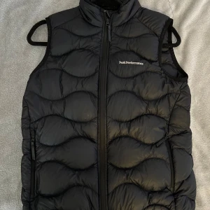 Svart dunväst från Peak Performance - Säljer min snygga och varma svarta dunväst från Peak Performance. Västen är i nyskick och säljes pga att den inte kommer till användning. Ordinare pris: 1300kr💕
