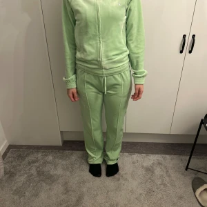 Set från Juicy Couture - Säljer en supermjuk och bekväm grön velour hoodie från Juicy Couture. Den har en dragkedja framtill och är dekorerad med glittriga stenar som bildar 'Juicy' på ryggen. Perfekt för en avslappnad dag eller en mysig hemmakväll. 38/M på båda. Byxor&tröja