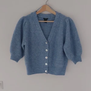 Blå stickad kofta från Lindex - Säljer en superfin blå stickad kofta från Lindex. Den har en v-ringad design med knappar framtill och trekvartsärmar. Perfekt för höst och vår när man vill ha något mysigt men ändå stilrent. Koftan är i storlek M och passar perfekt för en avslappnad look.
