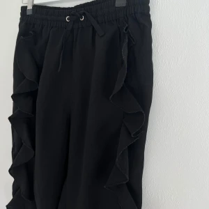 Byxor  - Svarta byxor med en söt volang längs benet, använda ett fåtal gånger och är därmed i fint skick! 🫶🏼