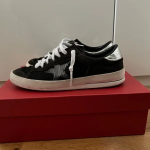 Svarta sneakers från Golden Goose - Snygga svarta sneakers från Golden Goose med silverdetaljer och vit sula. Skorna är modellen Super Dan. Skorna har en klassisk snörning och en unik design med märkets logga på hälen samt stjärnan på sidorna. Kommer utan låda. Har tecken på användning därav priset men väldigt sparsamt använda. 