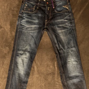 Replay x Barcelona Mörkblå jeansbyxor - Snygga mörkblå jeans med klassisk femficksdesign och kontrastsömmar. Byxorna har en dragkedja och knapp framtill samt en diskret logga på bakfickan. Perfekta för en avslappnad stil. Storlek W29 L32.