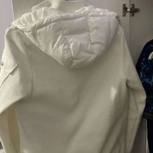 Vit dunjacka från Moncler - Säljer en stilren vit dunjacka från Moncler med avtagbar huva och dragkedja. Jackan har en quiltad design och långa ärmar, perfekt för kyliga dagar. Den är både snygg och funktionell, ett måste i garderoben! ❄️