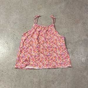 Blommig linne från H&M strl 134/140 - Färggladat blommigt linne från H&M i storlek 134/140. Linnet har smala axelband med rosetter på bandet och ett härligt mönster i rosa, lila och orange. Perfekt för varma sommardagar! 🌸