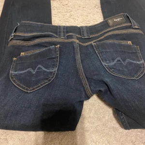 Mörkblå jeans från Pepe Jeans - Snygga mörkblå lågmidjade jeans från Pepe Jeans med klassisk femficksdesign och kontrasterande sömmar. Modellen är straight. 