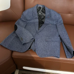 Blå kavaj från Friends-2 - Snygg blå kavaj från Friends-2 med ett diskret mönster. Kavajen har svarta armbågslappar och en innerficka med dragkedja. Perfekt för en stilren look.