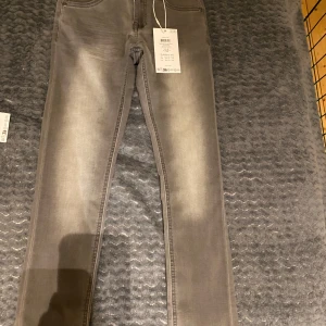Grå jeans från Name It - Snygga grå jeans från Name It i en slim passform. Perfekta för en stilren look med en medelgrå nyans. Byxorna har en klassisk design med dragkedja och knapp framtill.