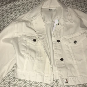 Vit jeansjacka från Gina Tricot  - Snygg vit jeansjacka från Perfect Jeans med klassisk design. Jackan har knappar framtill och två bröstfickor med knappdetaljer. Perfekt för vår och sommar!