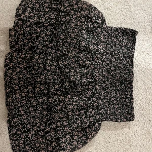 Svart blommig kjol - Söt svart kjol med små blommor i rosa och vitt. Kjolen har en elastisk midja som ger en bekväm passform. Perfekt för en avslappnad stil.