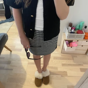 Svartvit rutig kjol - Snygg svartvit rutig kjol med klassiskt hundtandsmönster. Kjolen har en elastisk midja för bekväm passform och är perfekt för en stilren look. Den är knälång och passar bra till både vardag och mer uppklädda tillfällen.