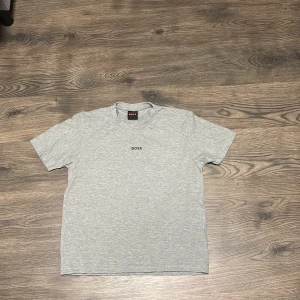 Grå t-shirt från Boss - Snygg grå t-shirt från Boss i bomull. Den har en enkel design med korta ärmar och rund halsringning. Perfekt för en avslappnad stil.