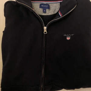 GANT mörkblå kofta - Säljer en stilren svart jacka från GANT med dragkedja och broderad logotyp på bröstet. Jackan har långa ärmar och ribbade muddar vid ärmslut och nederkant. Perfekt för en casual look.