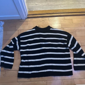 Svart och vit randig stickad tröja - Säljer en svart och vit randig stickad tröja med långa ärmar. Perfekt för kyligare dagar och ger en klassisk look. Tröjan har en bekväm passform och är lätt att matcha med olika outfits.