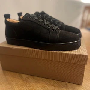 Christian Louboutin - Snygga svarta sneakers i mocka från Christian Louboutin med den ikoniska röda sulan. Skorna har snörning och en stilren design som passar perfekt för en trendig look.