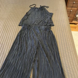 Svart plisserad jumpsuit från Shein storlek:XL - Snygg svart plisserad jumpsuit från Shein med halterneck och vida ben. Perfekt för en stilren look med en touch av elegans. Den har en glansig finish som ger en extra dimension till outfiten. Aldrig använd. Säljer för 150 kronor 