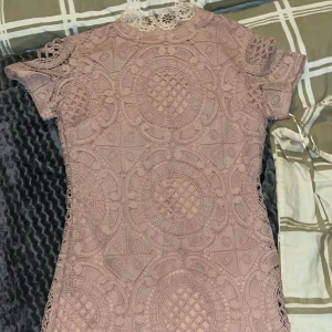 Rosa spetsklänning - Säljer en söt rosa spetsklänning från Girl In Mind. Klänningen har ett spetsmönster och korta ärmar. Den har en dragkedja i ryggen och en fin rund halsringning med spetsdetaljer. Perfekt för en romantisk look! 💖