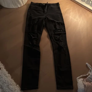 Svarta jeans med slitningar - Snygga svarta jeans med slitningar längs benen för en trendig look. De har en dragkedja och knapp i midjan. Perfekta för en avslappnad stil med en edgy touch. Passar perfekt till knä höga  boots eller stövlar!! 