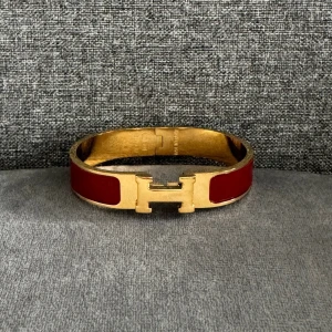 Rött armband med gulddetaljer - Elegant armband i röd färg med gulddetaljer och ett stilrent . Gjort av guld pläterat rostfritt stål  Perfekt för att ge en touch av lyx till din outfit. Helt nytt, st 16-17-18