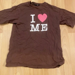 Brun t-shirt från Lager 157 - Säljer en brun t-shirt från Lager 157 med trycket 'I ❤️ ME' i vitt och rosa på framsidan. Perfekt för en självsäker look. T-shirten är kortärmad och gjord i ett mjukt material. Finns fett fläckar vid halsen och blekt sträck långst ner vid tröjan.