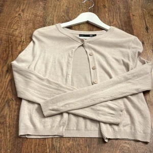 Beige kofta från 157 - Säljer en stilren beige kofta från 157 i storlek XS. Koftan har långa ärmar och knäpps med tre knappar framtill. Perfekt för lager-på-lager under kyligare dagar.