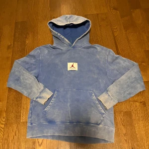 Nike Jordan Flight Hoodie - Säljer en blå hoodie från Jordan med en stor ficka fram och en Nike Flight-logga på ryggen. Tröjan har en klassisk hoodie-design med långa ärmar och en bekväm passform. Perfekt för en avslappnad stil. Lite urtvättad 