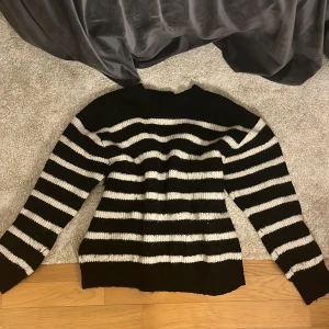 Svart och vit randig stickad tröja - Säljer en mysig svart och vit randig stickad tröja med långa ärmar. Perfekt för kyliga dagar och ger en stilren look. Tröjan har en ribbad krage och är både bekväm och trendig.