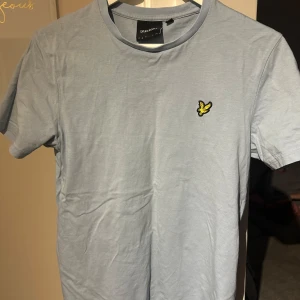 Ljusblå t-shirt från Lyle & Scott - Säljer en ljusblå t-shirt från Lyle & Scott med korta ärmar och en liten broderad logga på bröstet. Perfekt för en avslappnad stil. Tillverkad i mjukt bomullsmaterial.