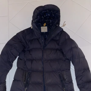 Svart dunjacka från Peak Performance - Säljer en svart dunjacka från Peak Performance med huva och dragkedja. Jackan har ett stilrent mönster på insidan och praktiska fickor med dragkedjor. Perfekt för kyliga dagar!