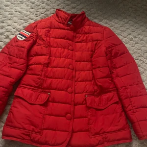 Röd quiltad jacka  - Snygg röd quiltad jacka med knappar och coola patches på ärmen. Jackan har en hög krage och praktiska fickor med knäppning. Perfekt för att hålla stilen när det är kyligt ute. Har två märken som går säkert bort att tvätta. Priset går att diskutera! 