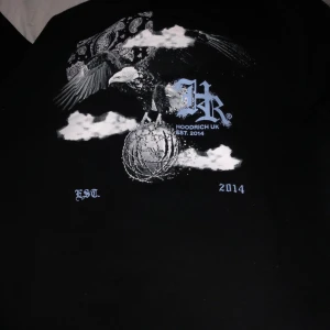 Svart hoodie  från Hoodrich UK - Snygg svart hoodie  från Hoodrich UK med tryck i vitt och blått. Designen inkluderar texten 'From Nothing To Something' och 'EST. 2014'. Perfekt för en cool och avslappnad stil.