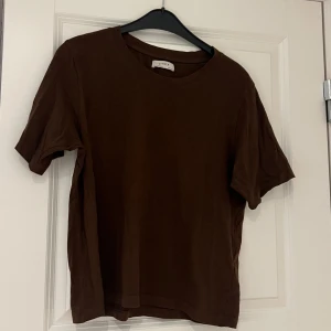 Brun t-shirt från Lindex - Säljer en enkel och stilren brun t-shirt från Lindex. Perfekt för en avslappnad look. T-shirten har korta ärmar och en rund halsringning.