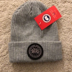 Grå ribbad mössa från Canada Goose - Snygg grå ribbad mössa från Canada Goose med ett broderat märke framtill. Perfekt för kyliga dagar. 449kr st! 
