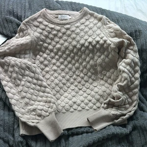 Beige stickad tröja från Only - Säljer en beige stickad tröja från Only med ett unikt mönster som påminner om fjäll. Tröjan har långa ärmar och ribbade muddar vid ärmslut och nederkant. Perfekt för kyliga dagar!