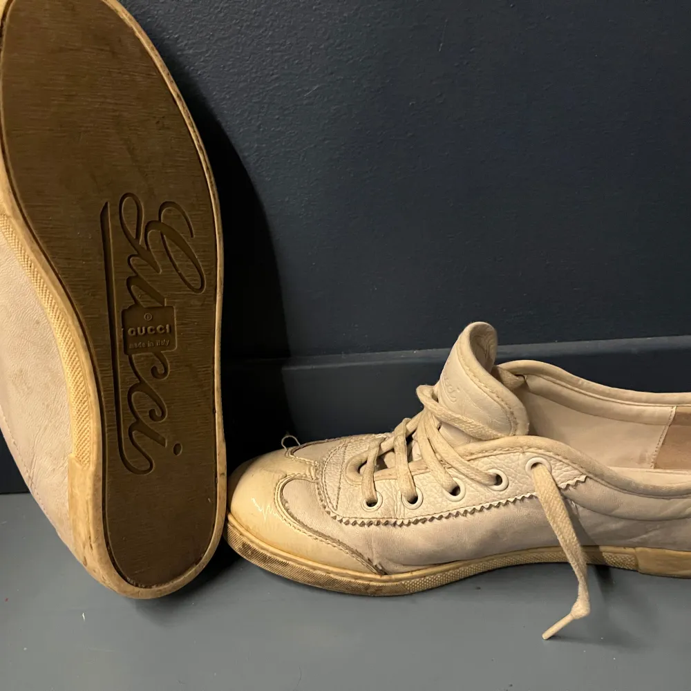 Snygga beige sneakers från Gucci med klassiska ränder i grönt och rött på sidan. Skorna har snörning och är tillverkade i skinn. Perfekta för en stilren look.lite smutsiga men väldigt snygga.. Kengät.