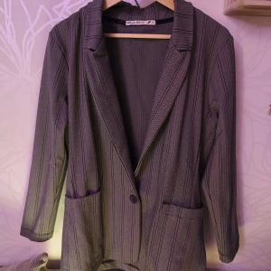 Grå randig kavaj från Black Story - Snygg grå kavaj från Black Story med diskreta ränder och en klassisk krage. Kavajen har långa ärmar och stängs med en knapp framtill. Perfekt för en stilren look.