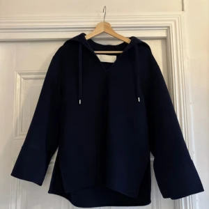 Mörkblå hoodie med huva - Säljer en stilren mörkblå hoodie med ”huva” och långa ärmar. Tröjan har en avslappnad passform och dragsko vid huvan. Perfekt för en casual look.