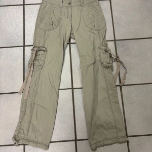 Beige cargopants med knytband - Snygga beige cargopants med flera fickor och knytband vid benen. Perfekta för en avslappnad stil med praktiska detaljer. Byxorna har en loose passform och är tillverkade i ett bekvämt material. Low waist