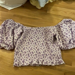 Lila blommig topp från Gina Tricot - Säljer en söt lila blommig topp från Gina Tricot. Toppen har puffiga kortärmar 🌸