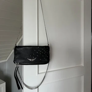 Zadig & Voltaire väska med hjärtan, stor modell. - Snygg svart axelväska i skinn från Zadig & Voltaire med hjärtan. Den är stor i modellen. Köpt den begagnad men jag har själv aldrig använt den! Väskan är i superfint skick det ända är att något av hjärtanen har någon liten difekt. Båda kedjorna ingår! 