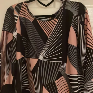 Mönstrad topp från Isolde - geometriskt mönster i svart, rosa och vitt. Toppen har trekvartsärmar och en rund halsringning. Storlek M