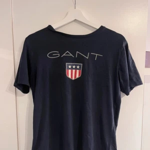 GANT t-shirt  - Säljer en mörkblå t-shirt från GANT från kidsbrandstore i storlek 170 cm (15år) men skulle säga det motsvarar storlek XS-S som jag i vanliga brukar ha. T-shirten har ett litet hål på sidan se bild 3 men annars i bra skick