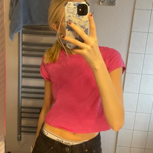 Rosa croppad t-shirt - Säljer en snygg rosa croppad t-shirt med korta ärmar. Perfekt för en avslappnad stil och passar bra till jeans eller shorts. Enkelt och stilrent plagg för vardagen.