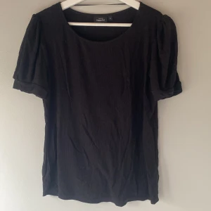 Svart topp från Kappahl - Säljer en stilren svart topp från Kappahl med korta ärmar och rund halsringning. Perfekt för en enkel och elegant look. Toppen är tillverkad i ett mjukt material som ger en bekväm passform.