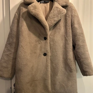Beige teddyjacka från Zara - Mysig beige teddyjacka från Zara med knappar framtill. Perfekt för kyliga dagar med sin fluffiga och varma design. Jackan har en klassisk krage och långa ärmar, vilket gör den både stilren och bekväm.
