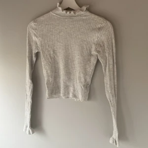 Grå ribbad polotröja - Säljer en stilren grå ribbad polotröja med långa ärmar och en elegant krage. Perfekt för kyligare dagar och lätt att matcha med olika outfits. Passar både till vardag och mer uppklädda tillfällen.