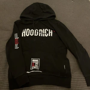 Svart hoodie från Hoodrich - Snygg svart hoodie från Hoodrich med tryck på bröstet och ryggen. Den har en stor huva och långa ärmar med tryck på ena ärmen. Perfekt för en avslappnad stil.