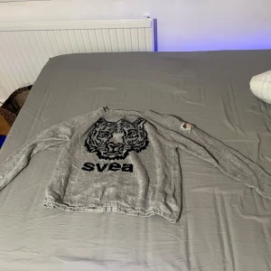 Grå tröja med tigertryck från Svea - Säljer en grå tröja från Svea med ett stort svart tigertryck på framsidan. Tröjan har långa ärmar och är i stl s nästan som ny använd några gånger bara
