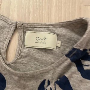 Grå klänning med hummermönster från Emma och Malena - Säljer en grå klänning med ett coolt hummermönster i mörkblått från Emma och Malena. Klänningen har långa ärmar och en avslappnad passform, perfekt för en chill dag. Den är gjord i mjukt bomullsmaterial och har en rund halsringning.